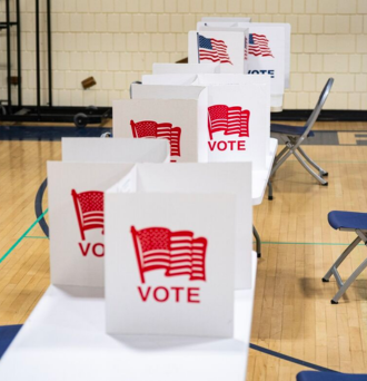 Photo of a voting booth with signs that read "VOTE" under an American flag